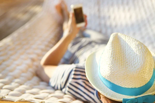 Mannen i hatten i en hängmatta med mobiltelefon en sommardag — Stockfoto