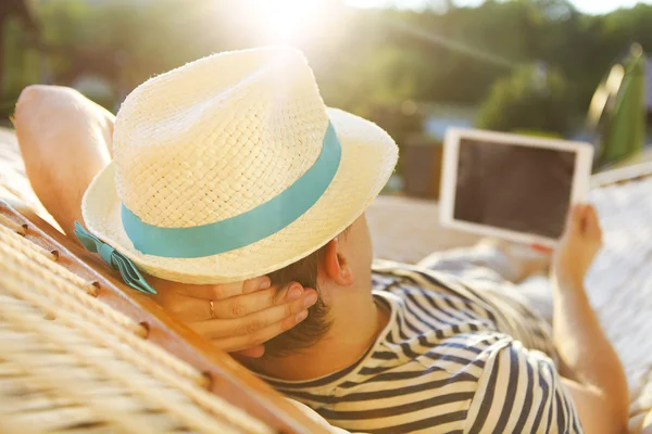 Mannen i hatten i en hängmatta med Tablet PC: n en sommardag — Stockfoto