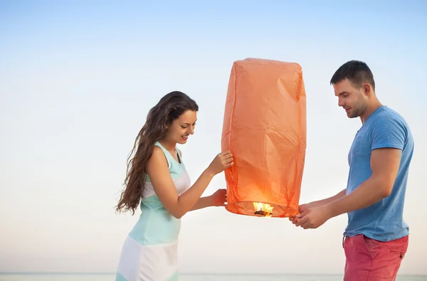 Couple start a red Chinese sky lantern in the dusk near the sea — Stock Photo, Image