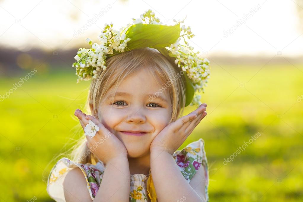 Cute little girl with blond hair in a wreath of lily of the vall