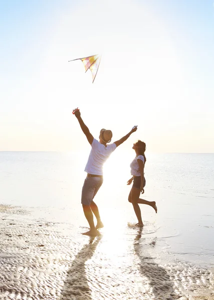 Jovem casal feliz com um papagaio voando na praia — Fotografia de Stock