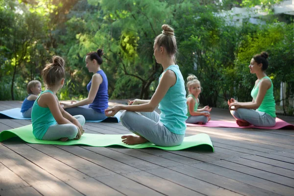 Grupp av mödrar och döttrar gör övning tränar yoga ou — Stockfoto