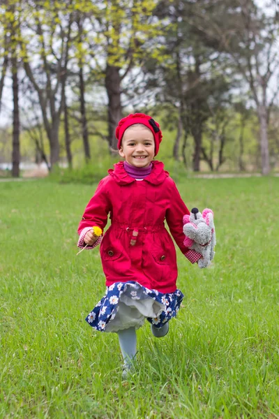 Красивая маленькая девочка в красной куртке и синем платье с цветами бежать — стоковое фото