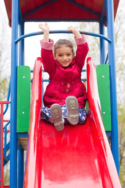 Little girl playing on playground in spring. Child in red jacket — Stock Photo, Image