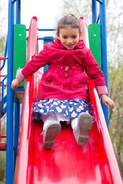 Little girl playing on playground in spring. Child in red jacket — Stock Photo, Image