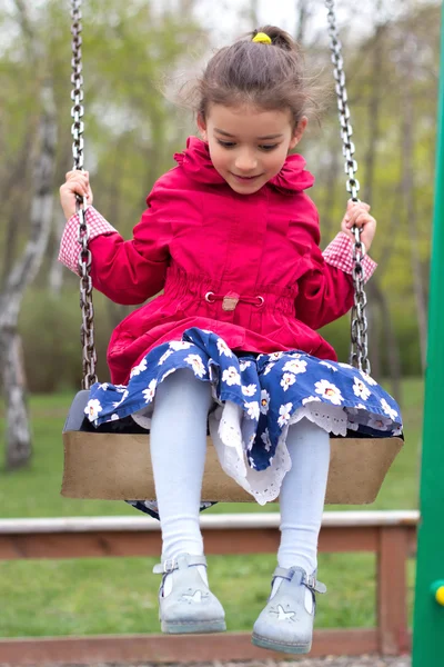 Cute little girl playing on playground in spring. Child in red j — Stock Photo, Image