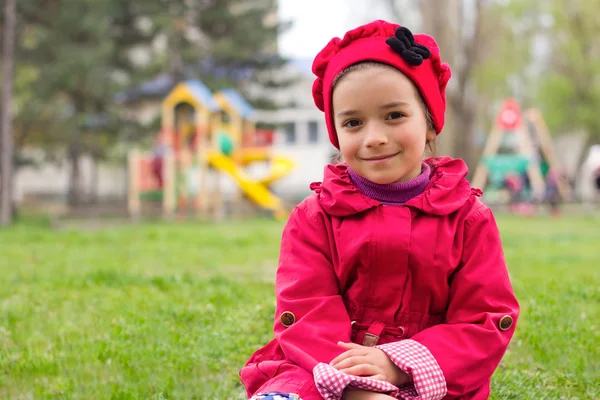 Little girl sitting on green grass on playground in spring. Chil — Stock Photo, Image