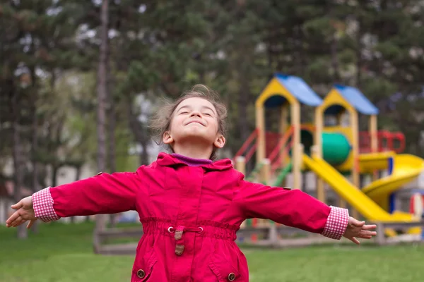 Little girl's joy on playground in spring. Child in red jacket i — Stock Photo, Image