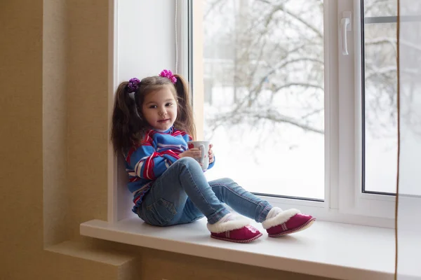 Pequeña chica de belleza con taza en la ventana — Foto de Stock