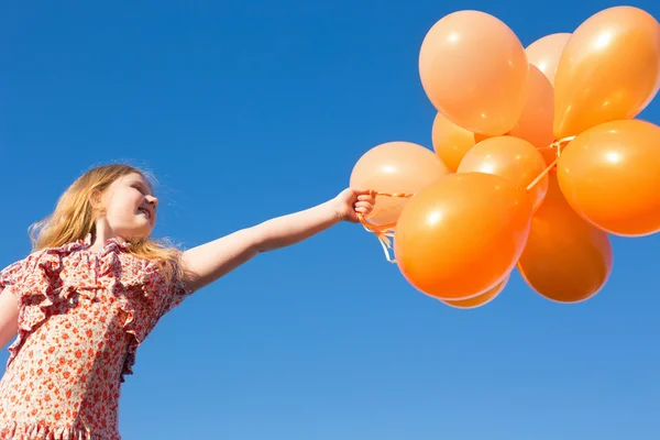 Glückliches Mädchen mit orangen Luftballons im Freien — Stockfoto