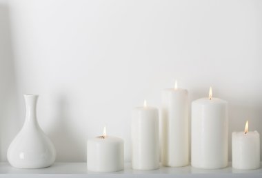 Beyaz bir rafa yanan beyaz mumlar