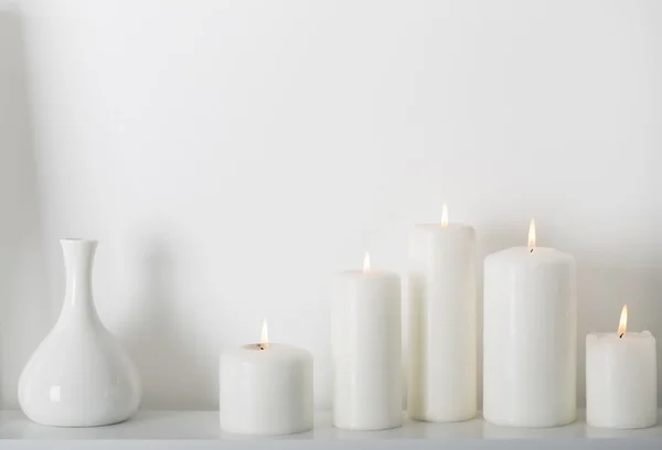 Velas brancas queimando em uma prateleira branca — Fotografia de Stock