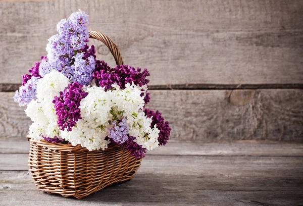 Basket with a branch of lilac flower on a wooden background — Stock Photo, Image
