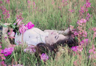 Çiçeklerle bir çayırda dinlenen kız.