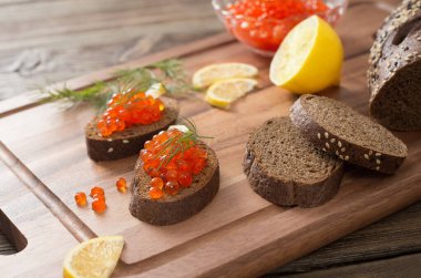 Tahtada siyah ekmek, dereotu ve limon olan kırmızı havyar.