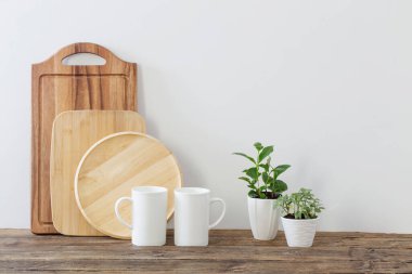 Ahşap tahtalar, beyaz bardaklar ve ahşap raflarda yeşil bitkiler.