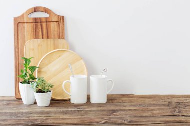 Ahşap tahtalar, beyaz bardaklar ve ahşap raflarda yeşil bitkiler.