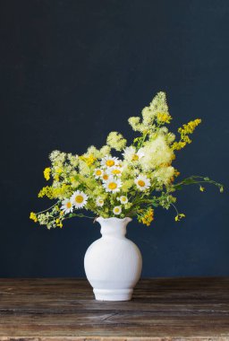 Beyaz vazodaki yabani çiçekler koyu arkaplanda