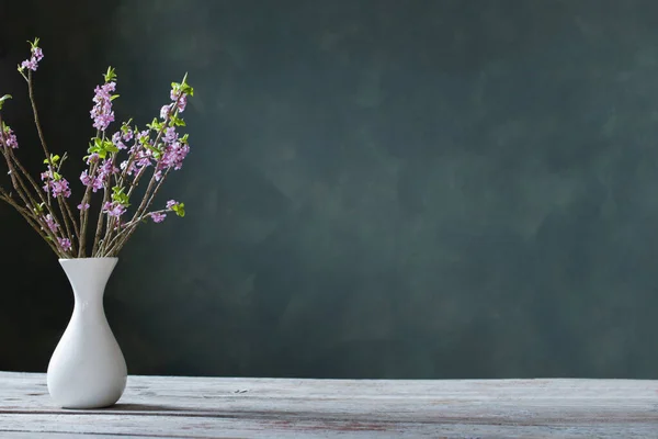 背景の緑の壁の古い木のテーブルの上の花瓶のダフネの花 — ストック写真