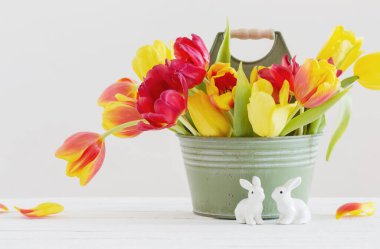 Kovada kırmızı ve sarı laleler ve beyaz arka planda seramik tavşan.