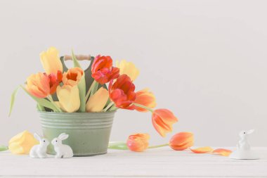 Kovada kırmızı ve sarı laleler ve beyaz arka planda seramik tavşan.