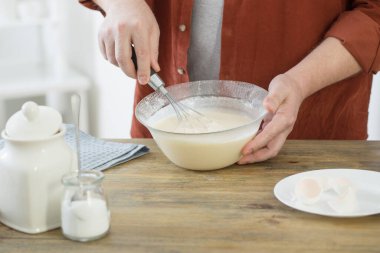 Beyaz mutfakta krep hamuru yoğuran orta yaşlı bir adam.