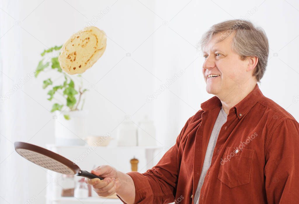 man flips  pancake in  air in kitchen