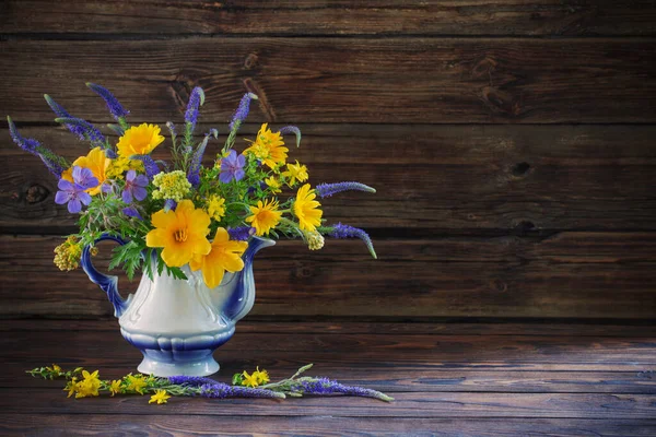 bouquet with blue and yellow flowers in teapot on wooden table