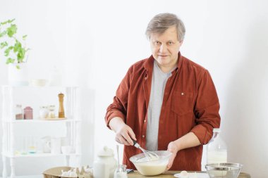 Beyaz mutfakta krep hamuru yoğuran orta yaşlı bir adam.