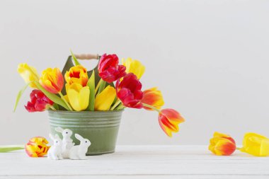 Kovada kırmızı ve sarı laleler ve beyaz arka planda seramik tavşan.