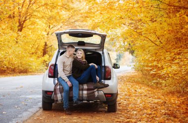 Sonbaharda yolda bir arabanın bagajında oturan genç çift.
