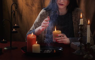Genç cadı karanlık arka planda yanan mumlarla büyüler yapıyor.