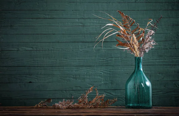 蓝色背景的木制桌子上玻璃花瓶里的干花 — 图库照片