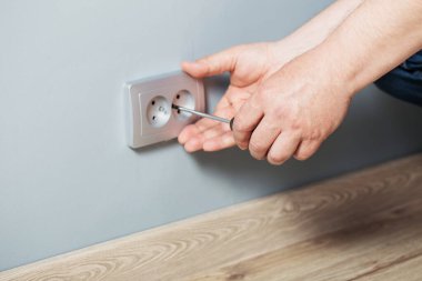 Adam gri duvara elektrik prizi takıyor.