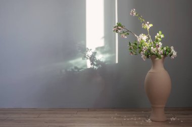 Elma ağacının dalları ve vazolarında gri duvarlar var.