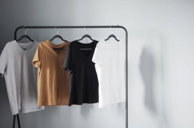 Gri duvara asılı siyah askı üzerine nötr renkli tişörtler