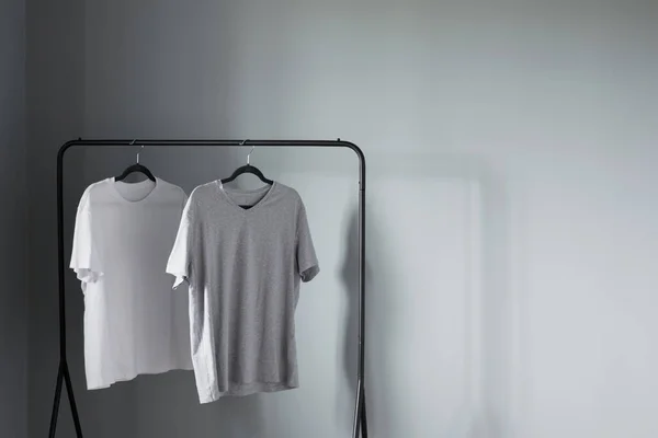 Deux Shirts Couleurs Neutres Sur Cintre Noir Contre Mur Gris — Photo