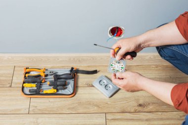 Adam gri duvara elektrik prizi takıyor.