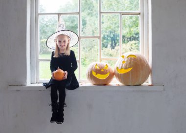 Cadılar bayramı balkabaklı siyah elbiseli küçük cadı pencere eşiğinde
