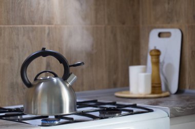 Gaz ocağında metal gümüş çaydanlık ve mutfakta mutfak gereçleri.