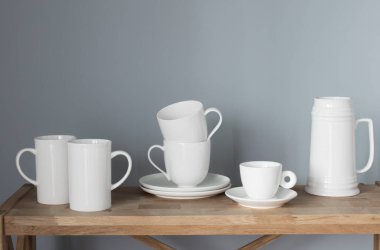 Beyaz bardaklar ve sürahiler gri arka plandaki ahşap rafta.