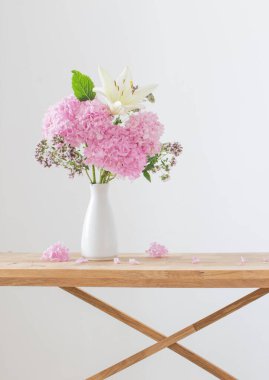 Beyaz vazodaki beyaz ve pembe çiçekler ahşap rafta.
