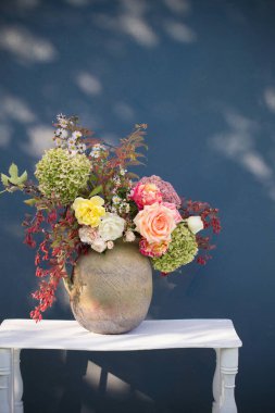 Kırsal seramik sürahi içinde sonbahar çiçekleri ve böğürtlenler arka planda mavi duvar