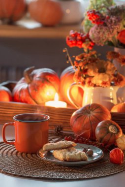 bir fincan portakal çayı ve sonbahar dekoru, balkabakları, çiçekler ve yanan mumlar.