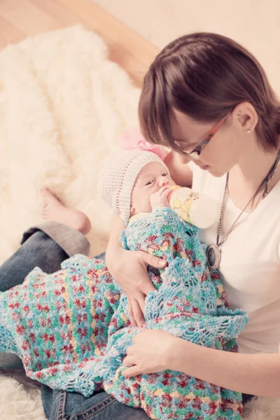 Mãe em casa alimentando sua nova menina com uma mamadeira de leite — Fotografia de Stock