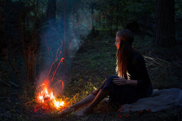 Beautiful witch looking at the fire in the forest