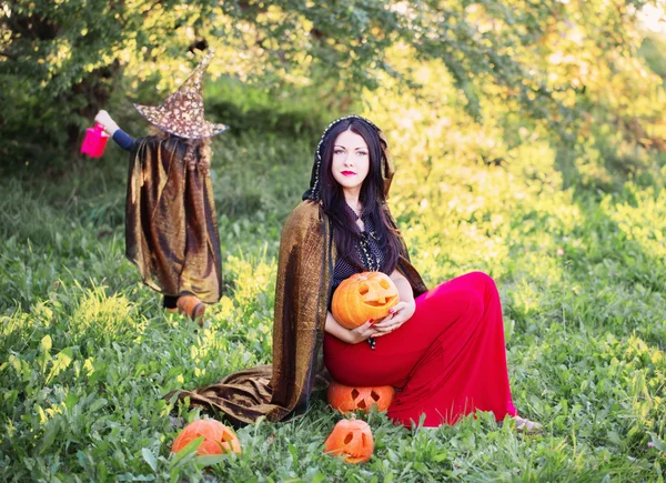 Moeder en dochter met pumpkins gekleed als heksen buiten — Stockfoto