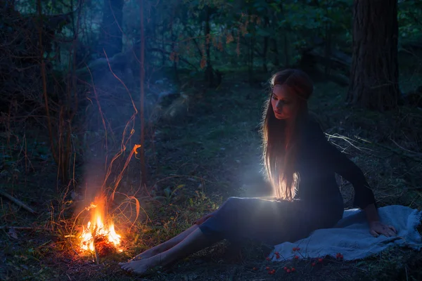 Beautiful witch looking at the fire in the forest — Stock Photo, Image