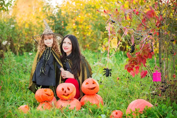 Moeder en dochter met pumpkins gekleed als heksen buiten — Stockfoto