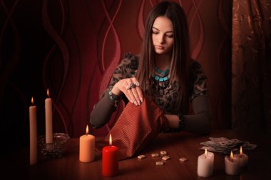 Young woman with runes and divination cards in room clipart